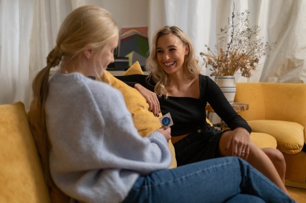 Woman in Blue Knit Sweater Holding Blue Condom Sitting Beside Woman in Black Dress